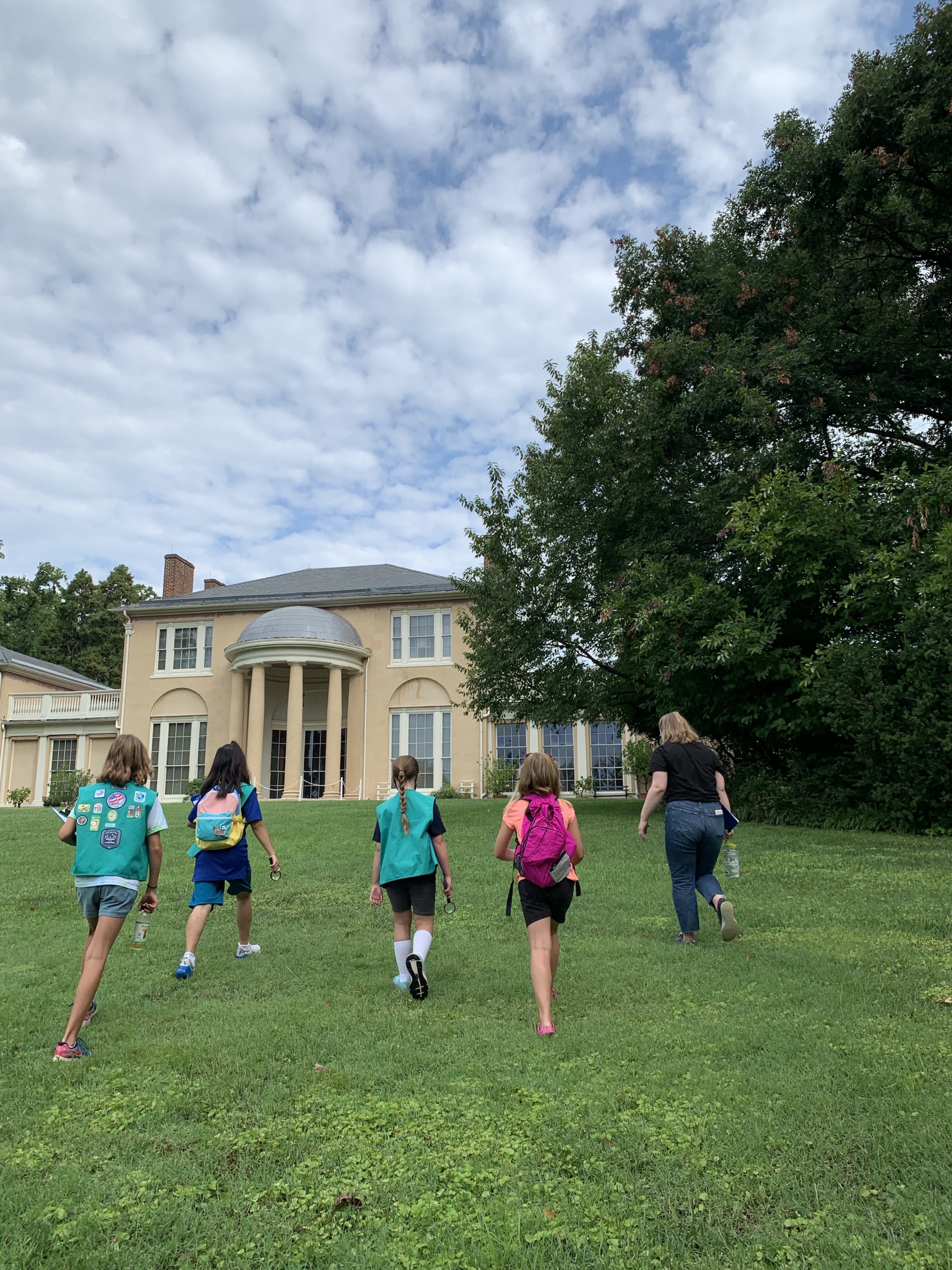 Girl Scouts walk up the South Lawn towards the historic house with their green Girl Scout sashes on.