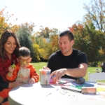 Mother holding child dressed in tiger costume with father at craft table