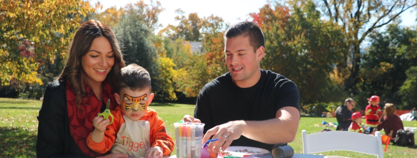 Mother holding child dressed in tiger costume with father at craft table