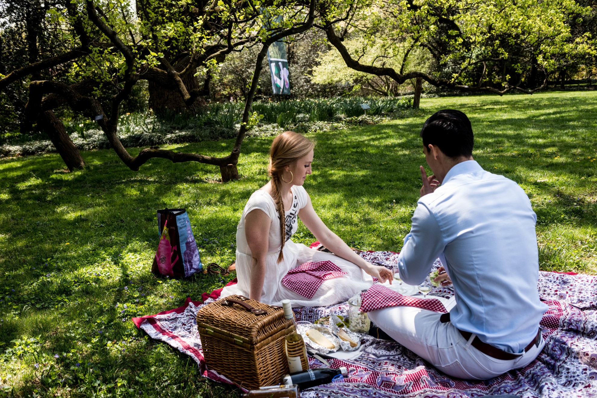 Couple sitting on read and white checkered blanket with brown wicker picnic basket