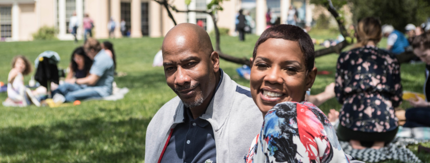 Close up of man and woman sitting on blanket enjoying sunshine at outdoor venue